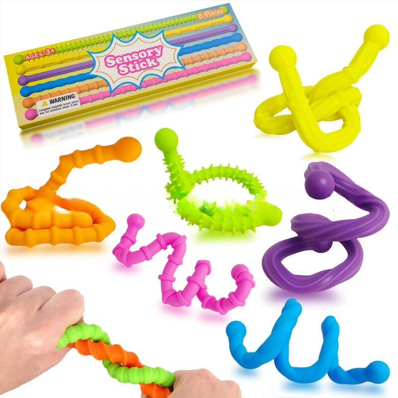 Na obrazie widoczne są kolorowe, giętkie wężyki sensoryczne o różnych fakturach i kształtach. Opakowanie z napisem \'Sensory Stick\' zawiera sześć sztuk, a na nim widnieje ostrzeżenie: \'WARNING: Choking hazard small parts. Not for children under 3 yrs.\'