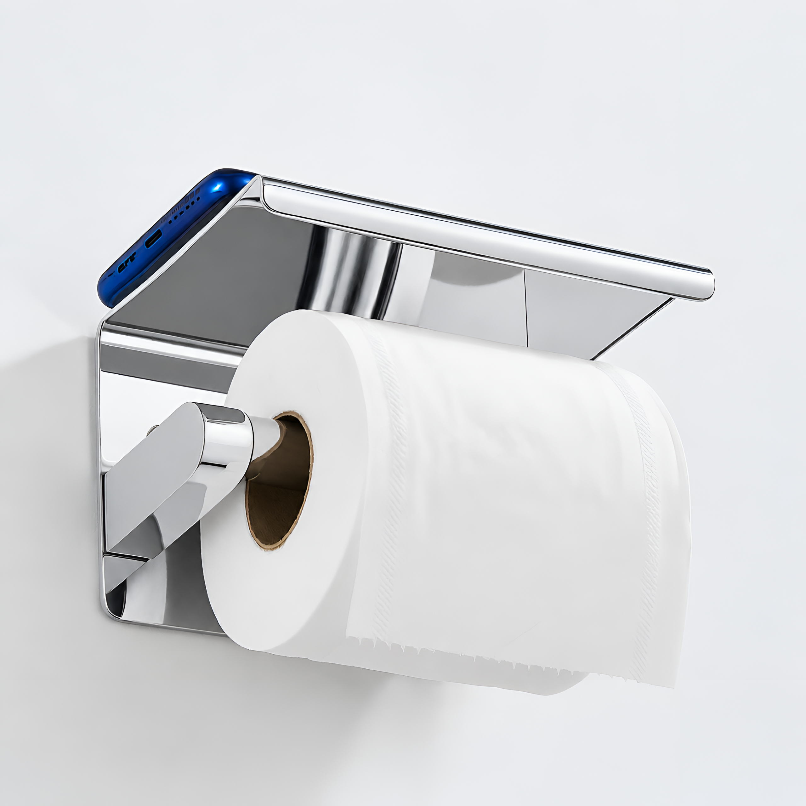 Metalowy uchwyt na papier toaletowy z półką, na której leży niebieski smartfon. Uchwyt jest chromowany i zamontowany na ścianie, trzymając rolkę papieru toaletowego.