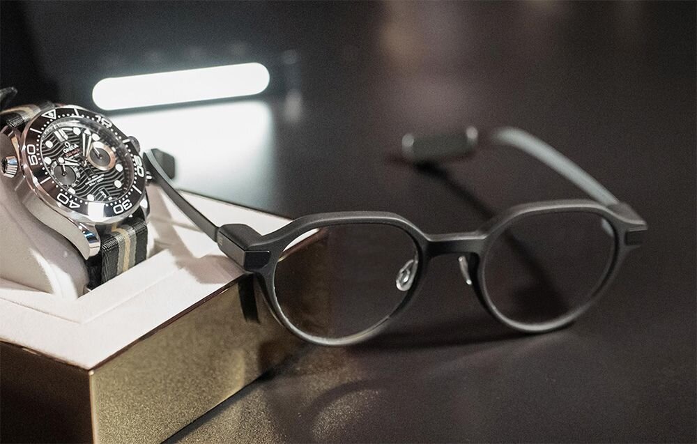 Czarne okulary leżące na ciemnym blacie tuż obok eleganckiego męskiego zegarka.