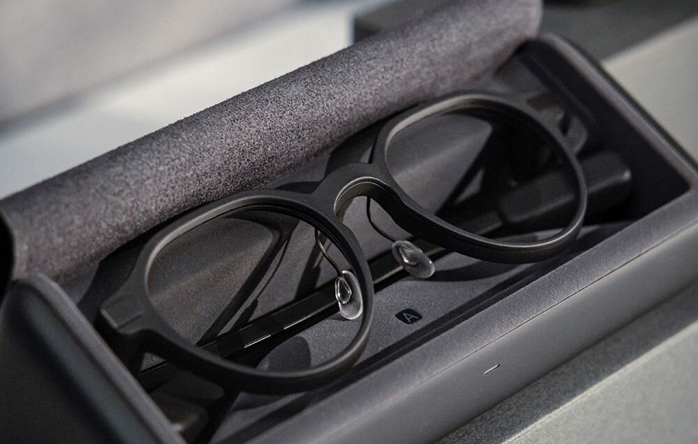 Czarno-szare okulary Even Realities spoczywające w otwartym etui ładującym.
