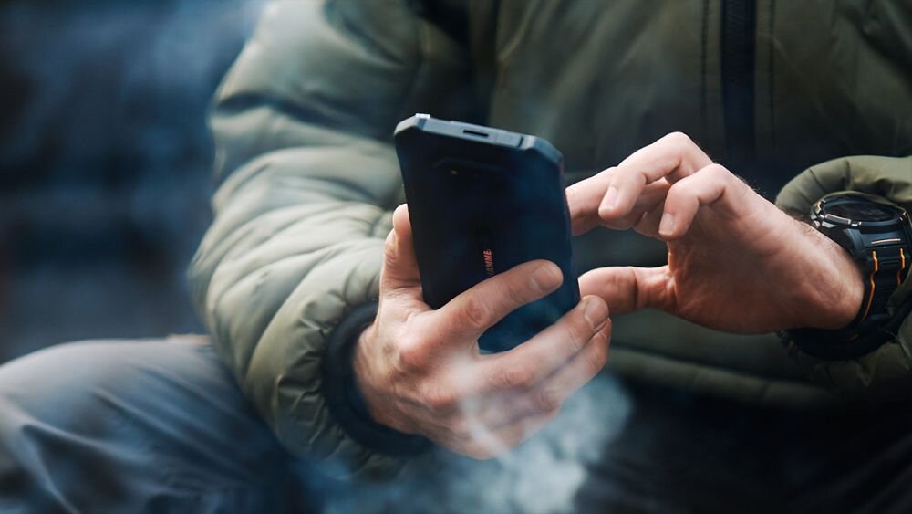 Osoba trzyma czarny smartfon, na którym widoczne jest logo \'HAMMER\'.
