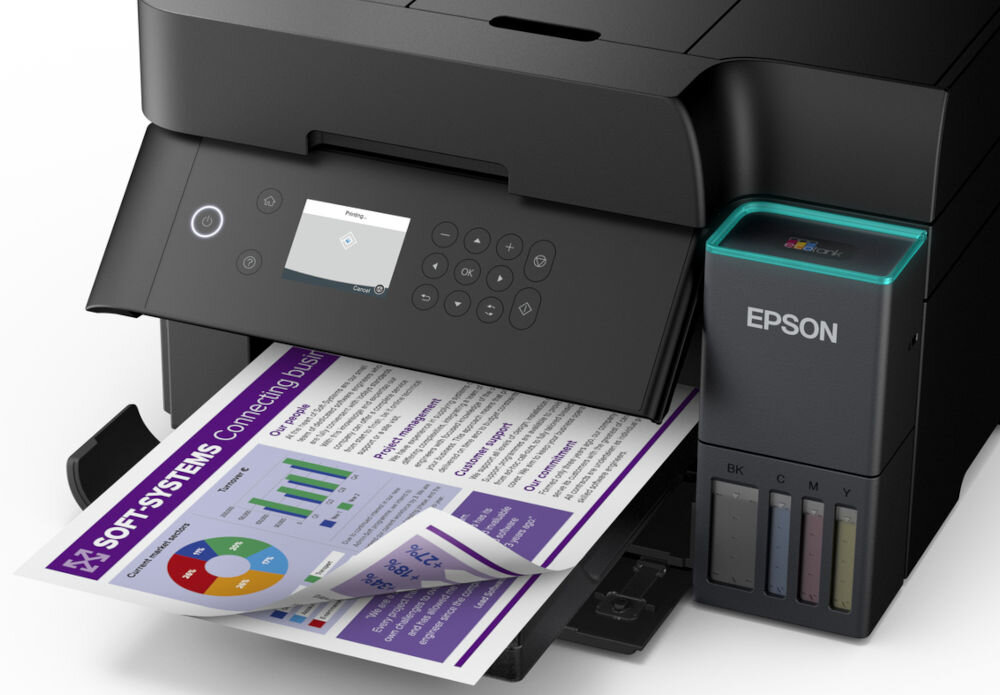 Na obrazie widoczne jest urządzenie wielofunkcyjne z logo EPSON, drukujące kolorowy dokument z wykresami i tekstem \'SOFT-SYSTEMS Connecting Business\'. Urządzenie posiada panel sterowania z przyciskami i wyświetlaczem oraz widoczne pojemniki na tusz oznaczone jako BK, C, M, Y.