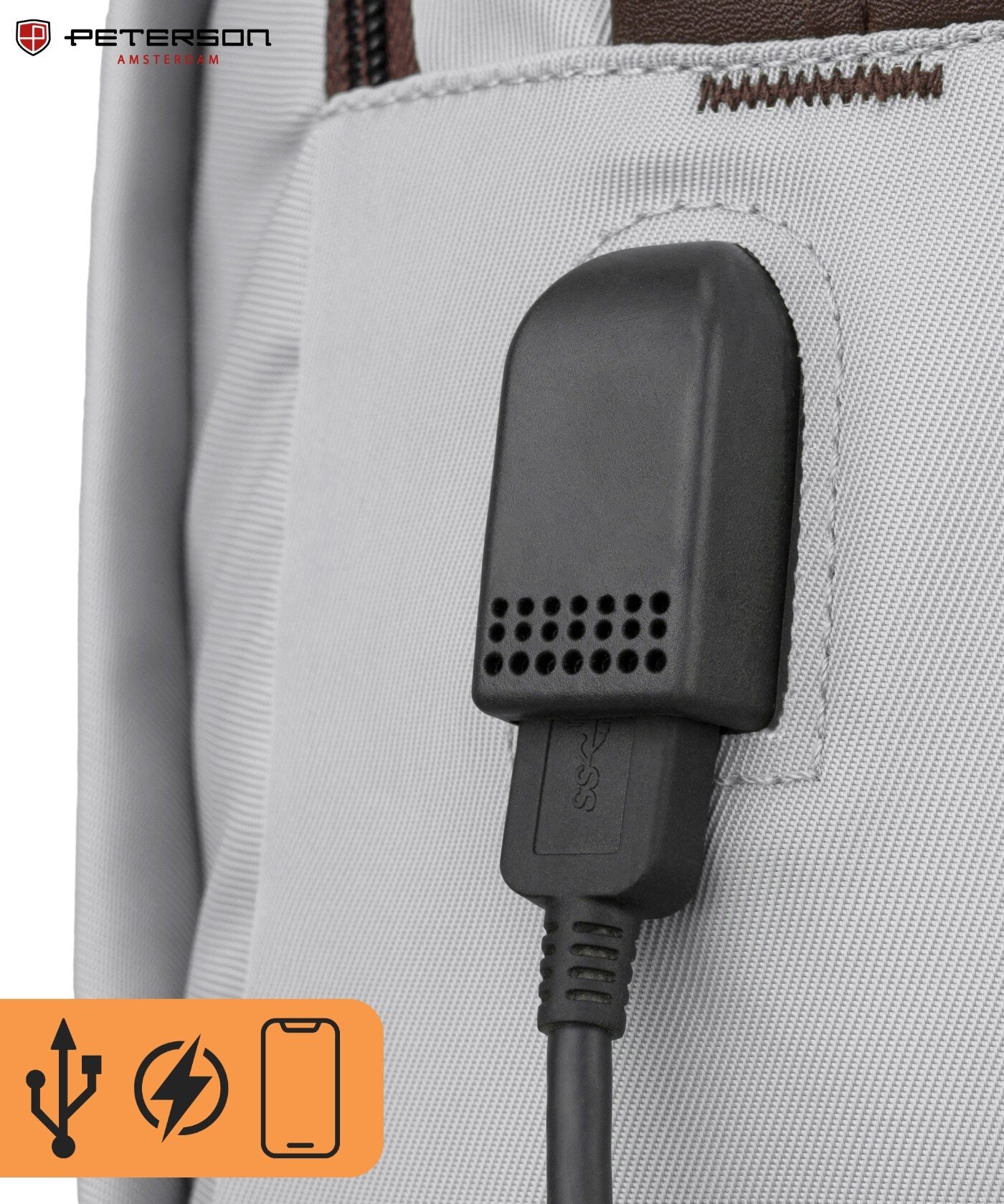 Zbliżenie na szary materiał plecaka z widocznym czarnym portem USB. W lewym górnym rogu znajduje się logo \'PETERSON AMSTERDAM\'.