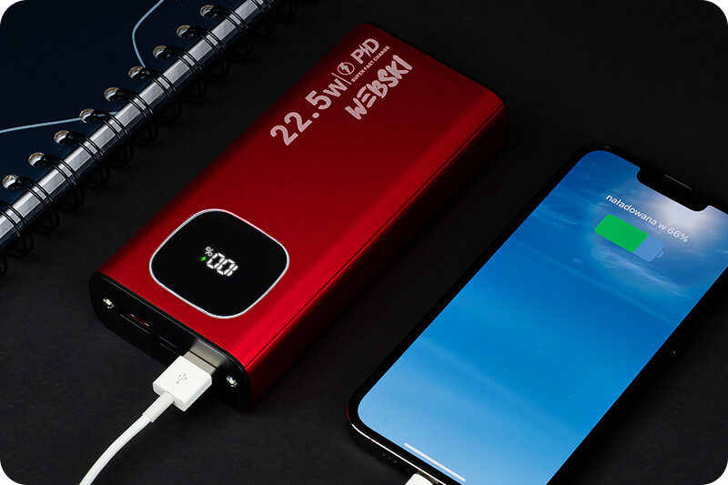 Czerwony powerbank z wyświetlaczem pokazującym 100% naładowania, obok smartfon z ekranem wskazującym \'naładowano w 66%\'. Na powerbanku widoczny jest napis \'22.5W PD WEBSKI\'.