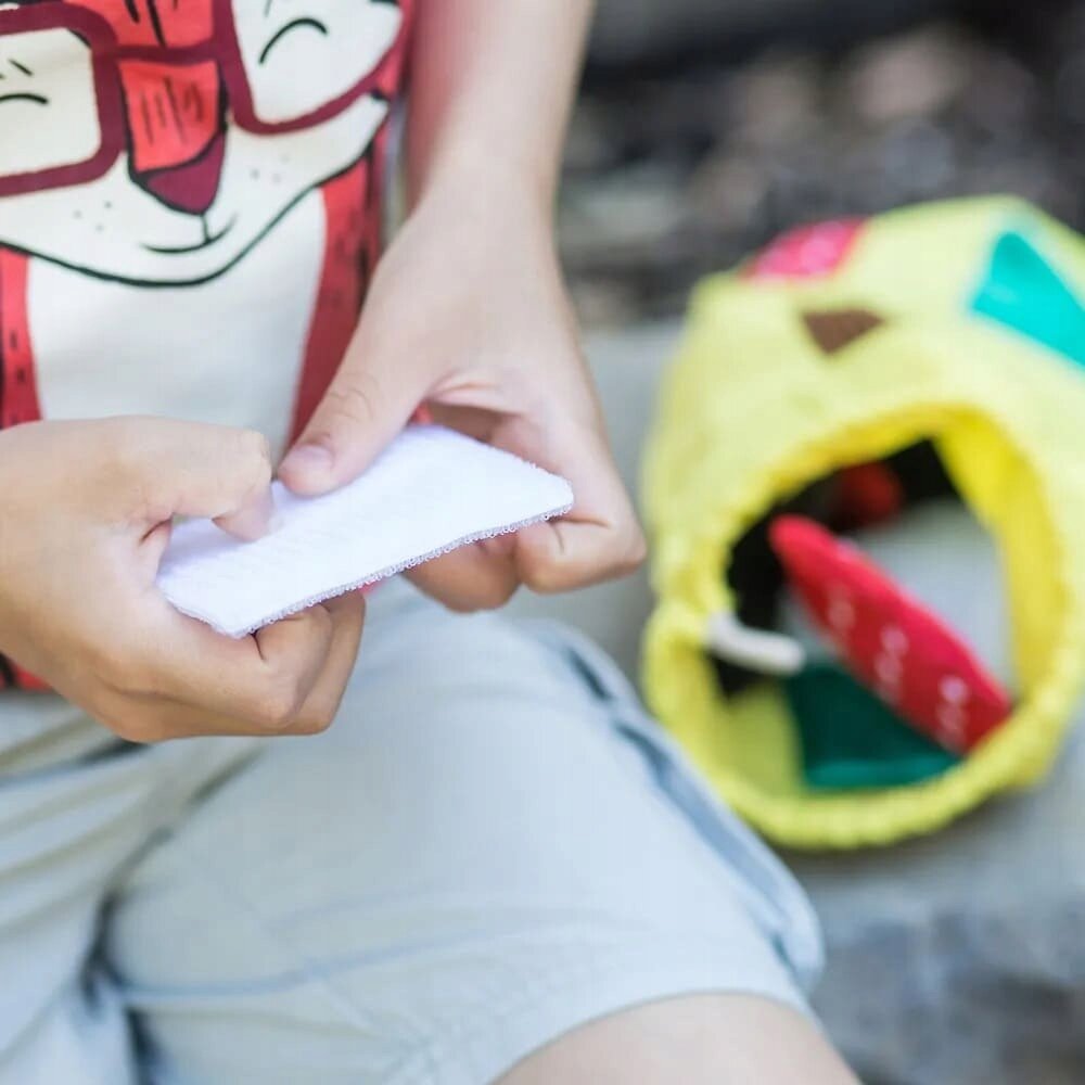 Osoba trzyma białą poduszeczkę dotykową, a obok znajduje się żółty worek z kolorowymi elementami w środku.