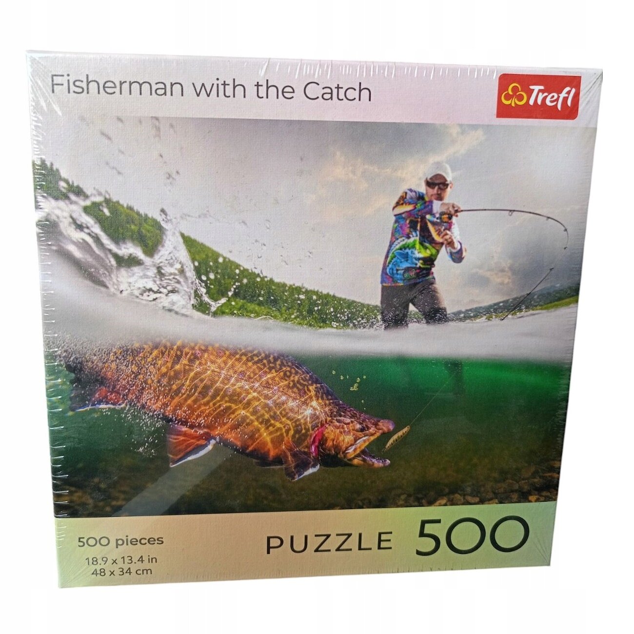 Opakowanie puzzli przedstawia wędkarza łowiącego rybę, z widocznym logo Trefl w prawym górnym rogu. Na dole opakowania znajduje się napis \'500 pieces 18.9 x 13.4 in 48 x 34 cm PUZZLE 500\'.