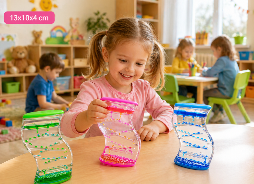Dziecko bawi się trzema sensorycznymi klepsydrami w kolorach zielonym, różowym i niebieskim, siedząc przy stole w przedszkolu. W tle widać inne dzieci zajmujące się różnymi aktywnościami oraz napis \'13x10x4 cm\'.