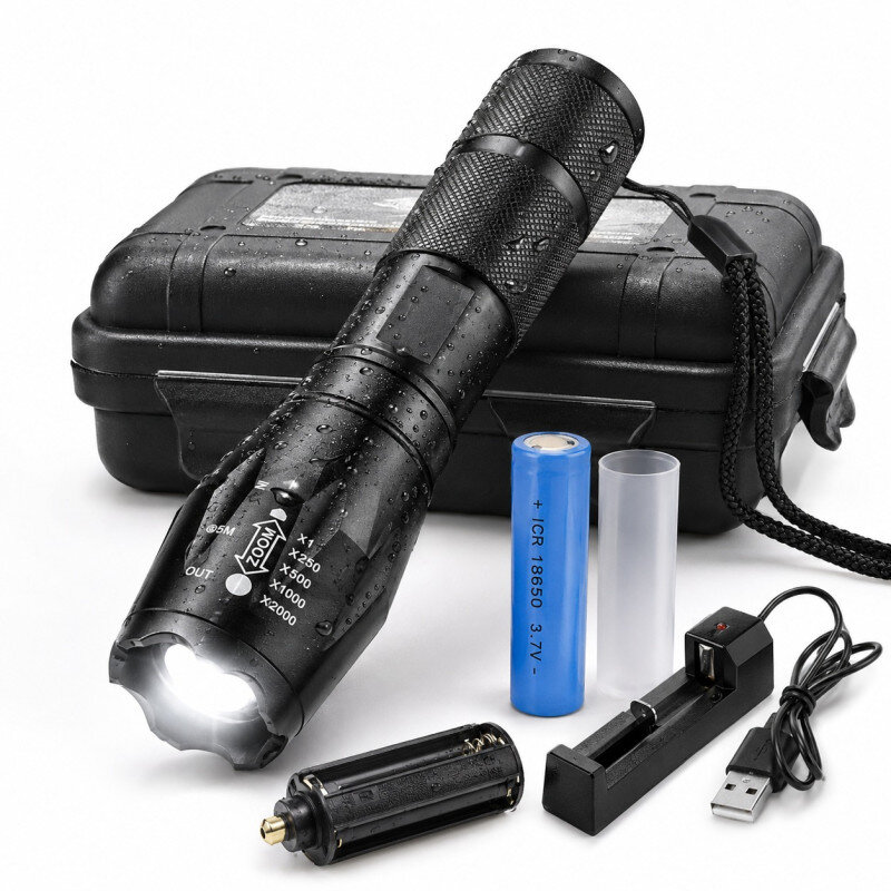 Na obrazie znajduje się czarna latarka LED z widocznymi kroplami wody, obok której leży niebieska bateria, przezroczysta tuleja, ładowarka USB oraz czarne etui. Na latarce widoczny jest napis \'ZOOM\' oraz oznaczenia powiększenia.