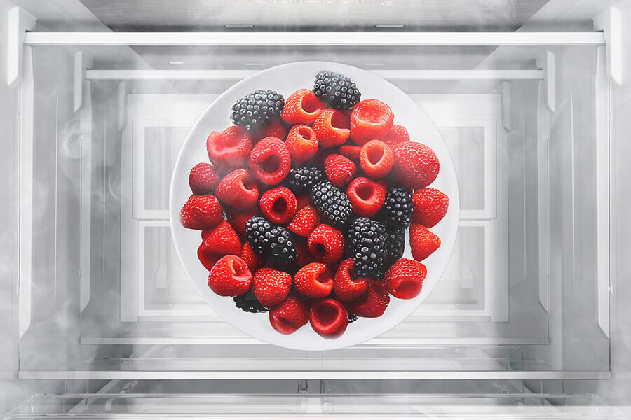 No Frost - Samsung lodówka - Media Expert Na obrazie widoczny jest talerz z malinami i jeżynami umieszczony wewnątrz lodówki. Wokół talerza unosi się delikatna mgiełka, sugerująca chłodne środowisko.