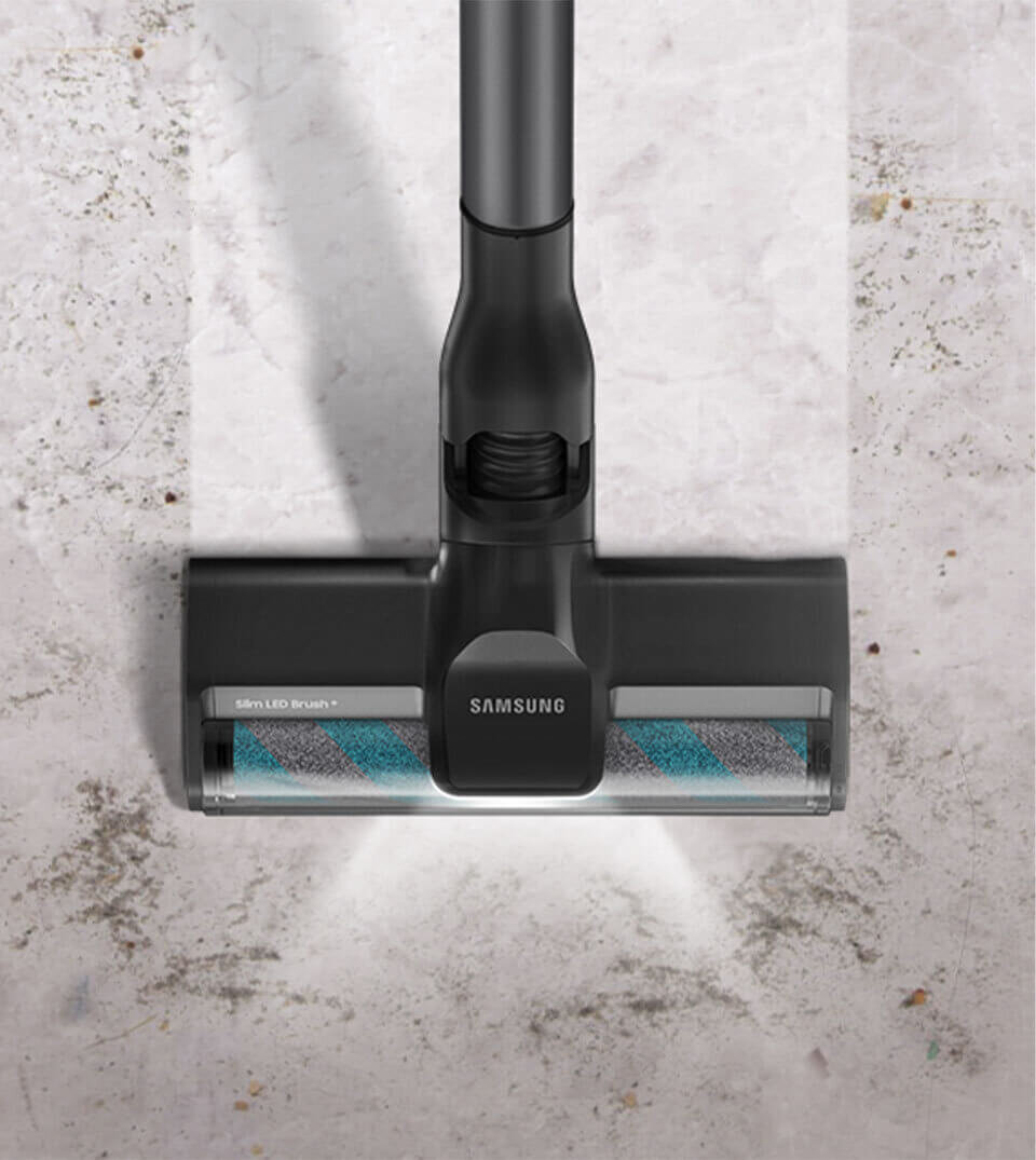 Na obrazie widoczna jest głowica odkurzacza z napisem \'SAMSUNG\' oraz \'Slim LED Brush+\'. Odkurzacz znajduje się na jasnej, lekko zabrudzonej podłodze.