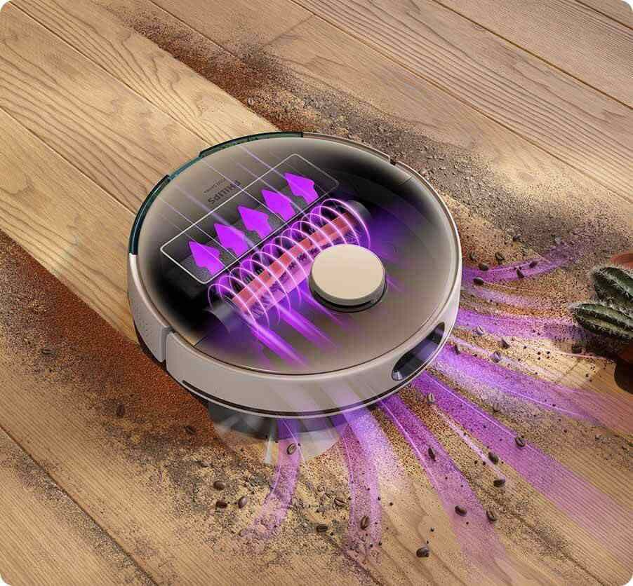 Robot sprzątający na drewnianej podłodze, otoczony przezroczystymi i fioletowymi strumieniami powietrza, zbiera rozsypane zanieczyszczenia. Na urządzeniu widoczne jest logo \'PHILIPS\'.