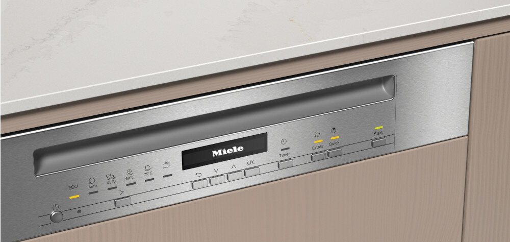 Panel sterowania zmywarki z widocznym logo \'Miele\' oraz przyciskami i wskaźnikami LED. Panel jest wbudowany w drewnianą zabudowę kuchenną.