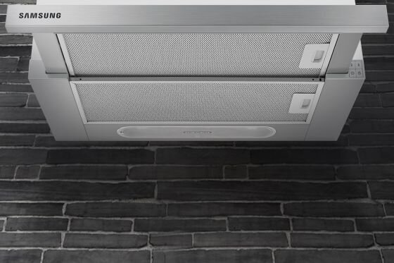 Samsung Wytrzymałość i trwałość na lata. Aluminiowe filtry Na obrazie widoczny jest okap kuchenny w kolorze stali nierdzewnej z logo \'SAMSUNG\'. Okap zamontowany jest na tle ściany z ciemnych cegieł.