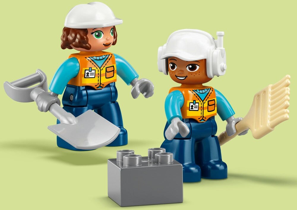 Na obrazku znajdują się dwie figurki LEGO w kaskach i kamizelkach, trzymające narzędzia budowlane. Przed nimi leży szary klocek LEGO.