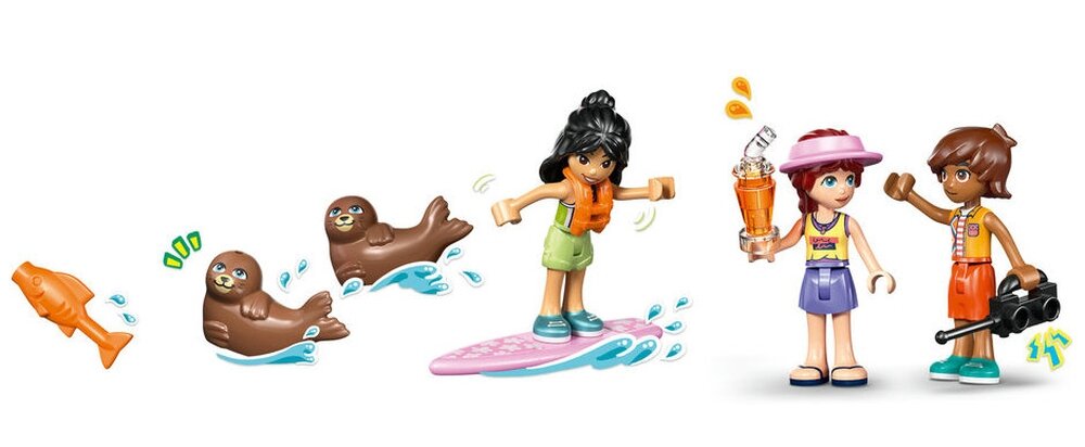 Na obrazku znajdują się figurki LEGO przedstawiające dwie postacie ludzkie oraz dwie foki i rybę. Jedna z postaci stoi na desce surfingowej, a druga trzyma napój i aparat fotograficzny.