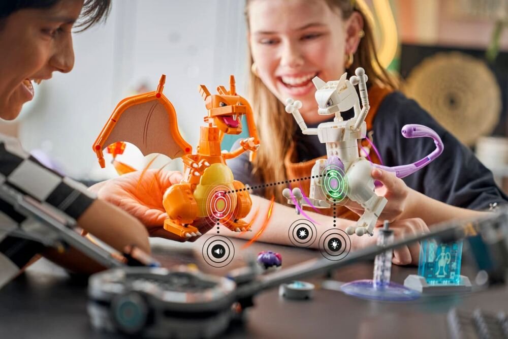 Dwoje dzieci bawi się zestawem LEGO z figurkami przypominającymi smoka i robota. Na stole widoczne są elementy konstrukcyjne i interaktywne symbole.