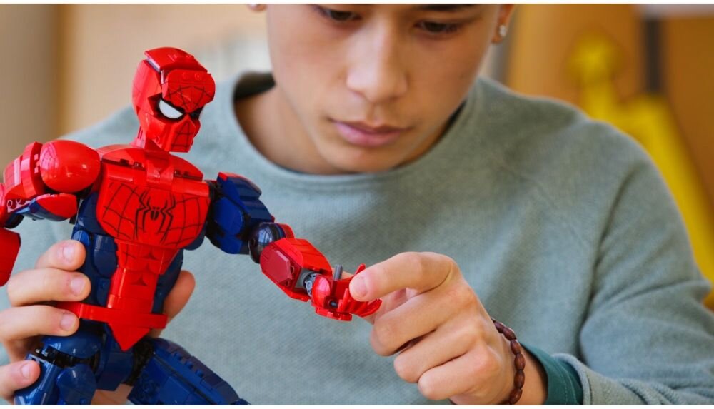 Osoba trzyma dużą figurkę Spider-Mana z czerwonym i niebieskim kostiumem, z widocznym symbolem pająka na klatce piersiowej.