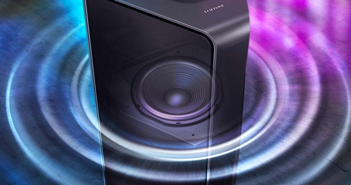 Głośnik z widocznym logo \'SAMSUNG\' emituje kolorowe fale dźwiękowe na podłodze. Otoczenie jest oświetlone niebieskimi i fioletowymi światłami.
