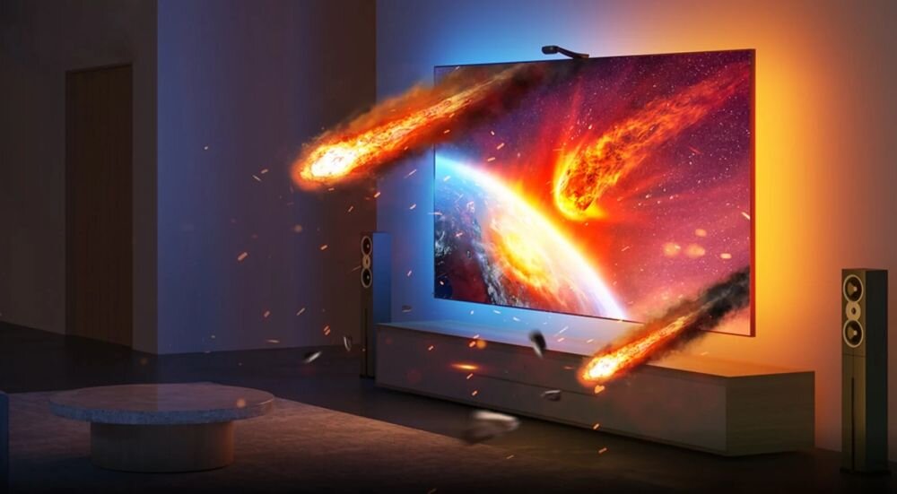 Telewizor wyświetla dynamiczną scenę z kosmosu z płonącymi meteorytami, a za nim widoczne jest kolorowe podświetlenie LED. W pomieszczeniu znajdują się również głośniki i okrągły stolik.