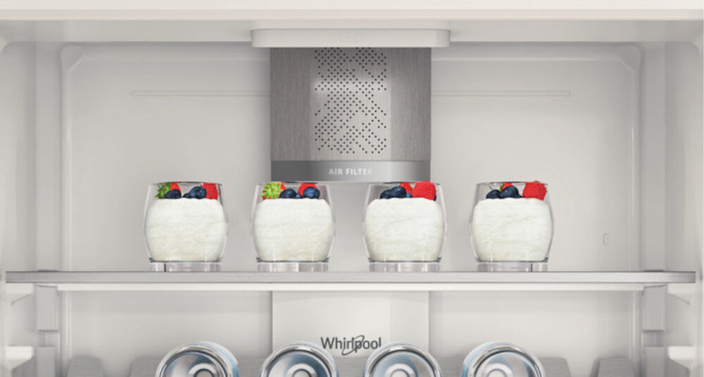 Wnętrze lodówki z czterema szklankami wypełnionymi białą substancją i owocami na górze. Widoczne logo \'Whirlpool\' oraz napis \'AIR FILTER\'.