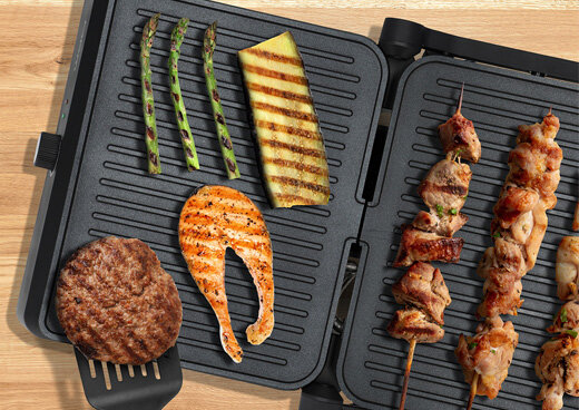 Na grillu elektrycznym kontaktowym  ułożone są szaszłyki z mięsa, grillowany stek, filet z łososia