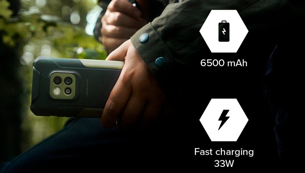 Osoba trzyma smartfon w czarno-zielonej obudowie. Obok widoczne są ikony z tekstem: \'6500 mAh\' i \'Fast charging 33W\'.