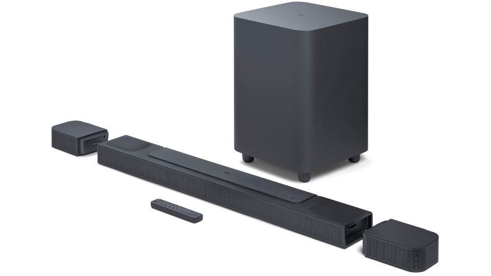 Na obrazie widoczny jest czarny soundbar z bezprzewodowym subwooferem oraz dwoma mniejszymi głośnikami. Obok znajduje się pilot do sterowania urządzeniem.