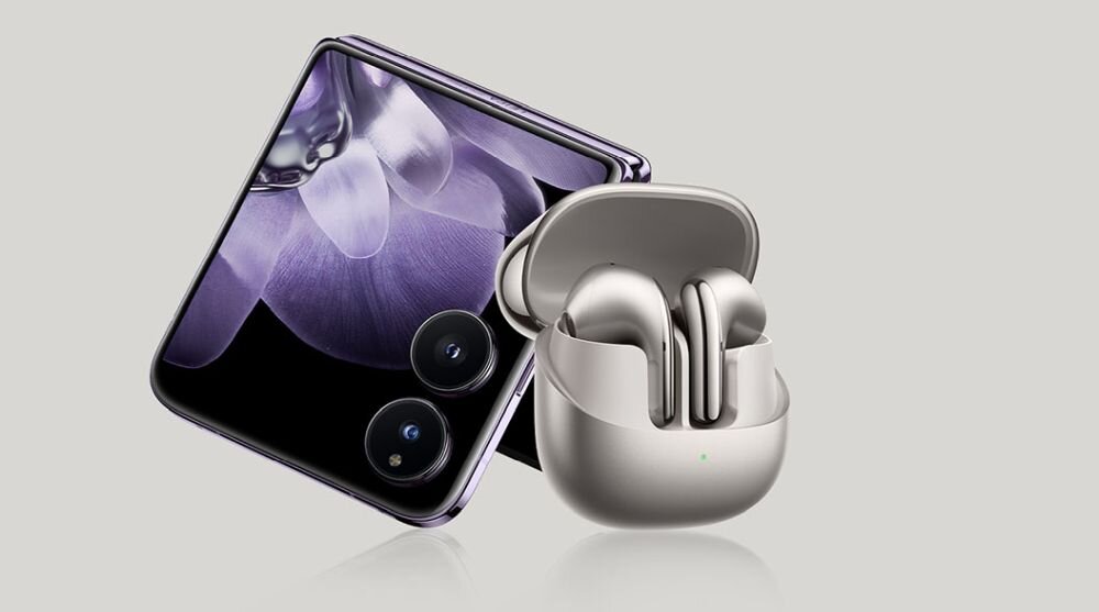 Na obrazie widoczny jest smartfon z wyświetlaczem przedstawiającym fioletowy kwiat oraz etui z otwartymi słuchawkami bezprzewodowymi w kolorze srebrnym.