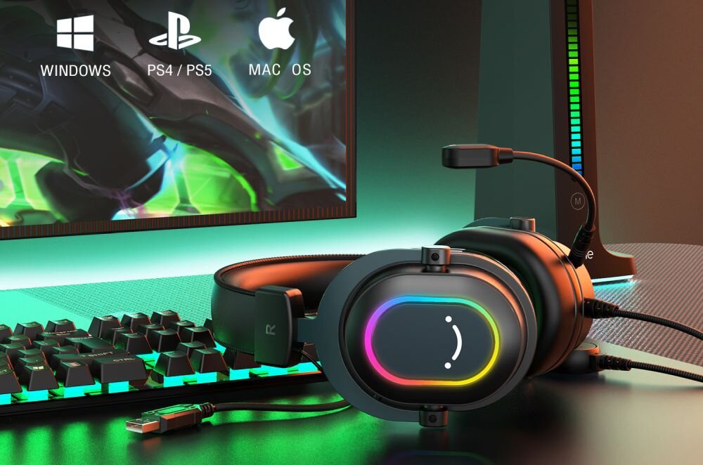 Na obrazie widoczne są czarne słuchawki z podświetleniem RGB, leżące obok klawiatury i monitora. Na ekranie monitora znajdują się ikony systemów: Windows, PS4/PS5, Mac OS.