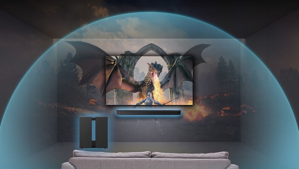 W pokoju znajduje się telewizor wyświetlający obraz smoka ziejącego ogniem, a pod nim umieszczony jest soundbar. Obok telewizora stoi czarny subwoofer, a całość otacza niebieska poświata sugerująca efekt dźwięku przestrzennego.
