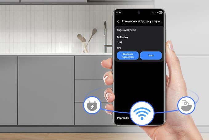 Sterowanie zmywarką przez aplikację mobilną – ekran z wyborem cyklu na smartfonie w nowoczesnej kuchni Osoba trzyma smartfon z aplikacją pokazującą \'Przewodnik dotyczący zmywarki\', sugerowany cykl \'Delikatny\' z czasem 1:57 i przyciskami \'Opóźnione rozpoczęcie\' oraz \'Start\'. W tle widoczna jest nowoczesna kuchnia z szarymi szafkami i białymi płytkami na ścianie.