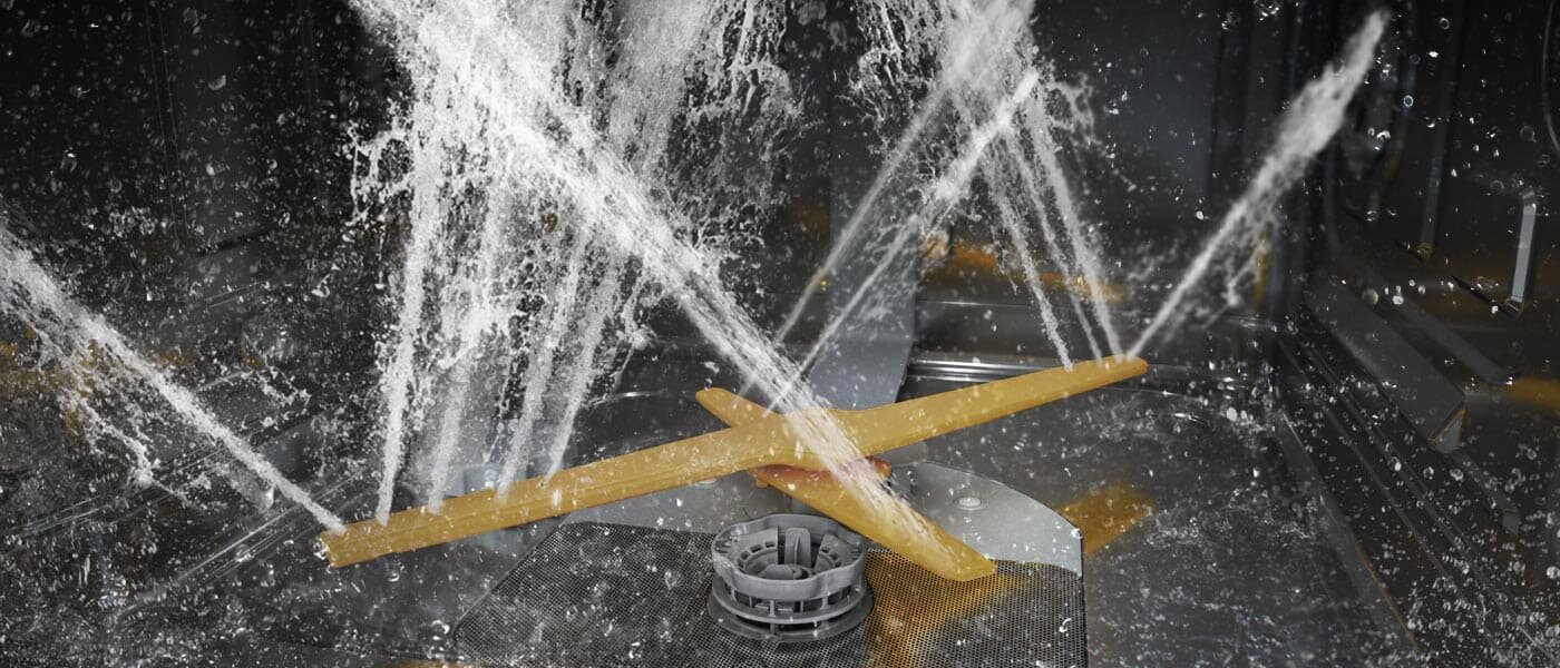zmywarka Samsung dw60dg790b00u1 z technologią waterjet clean Wnętrze zmywarki z widocznymi strumieniami wody rozpryskującymi się na plastikowym elemencie w kształcie litery X.