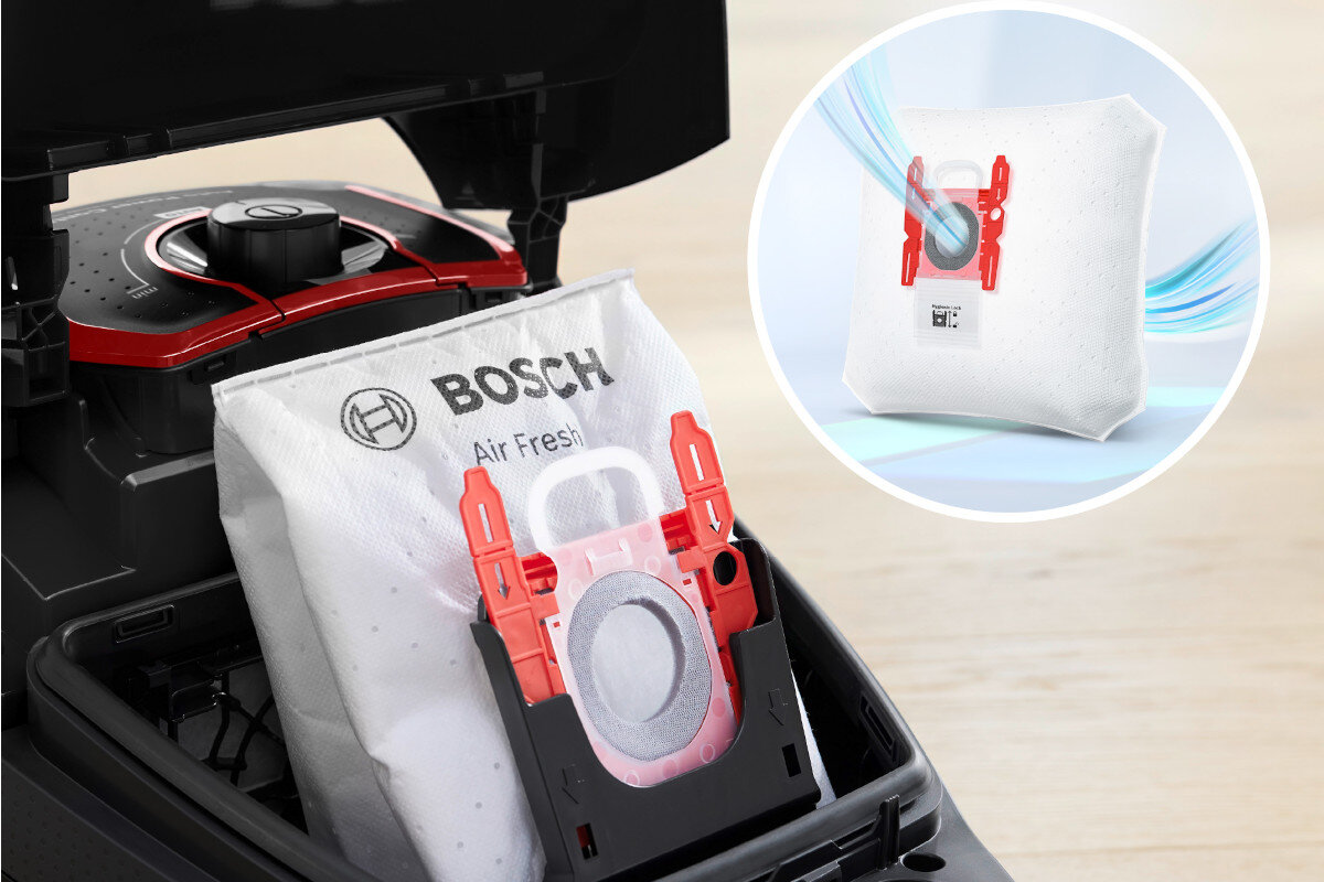 Odkurzacz z otwartą komorą na worek, w której znajduje się biały worek z napisem \'BOSCH Air Fresh\' i czerwonym uchwytem. Obok widoczna jest grafika przedstawiająca ten sam worek z efektem przepływu powietrza.