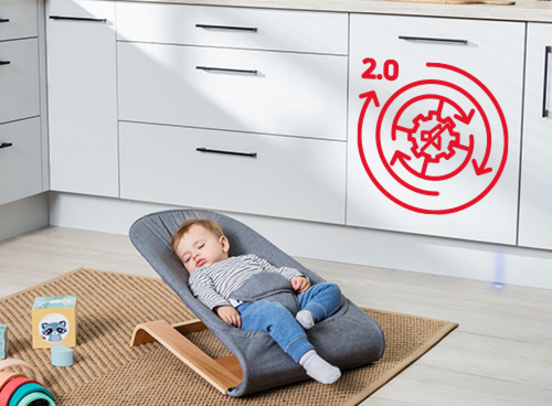 Na podłodze w kuchni leży dziecko w foteliku, a na szafce kuchennej widoczny jest czerwony symbol z napisem \'2.0\' przedstawiający mechanizm zębaty z przekreśleniem.