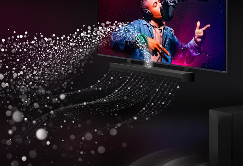Obraz przedstawia telewizor z osobą śpiewającą do mikrofonu oraz soundbar umieszczony pod ekranem. Wokół soundbara widoczne są efekty wizualne przypominające fale dźwiękowe.
