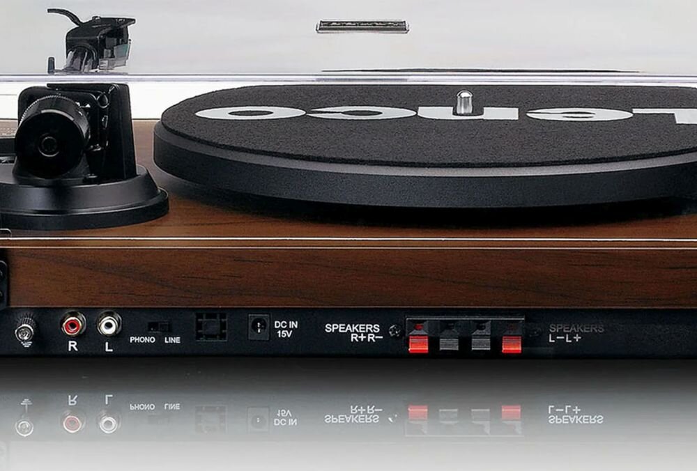 Gramofon z drewnianą obudową i czarną matą z napisem \'lenco\' na talerzu. Widoczne są złącza audio, w tym R L, PHONO, LINE, oraz gniazda głośnikowe i zasilania DC IN 15V.