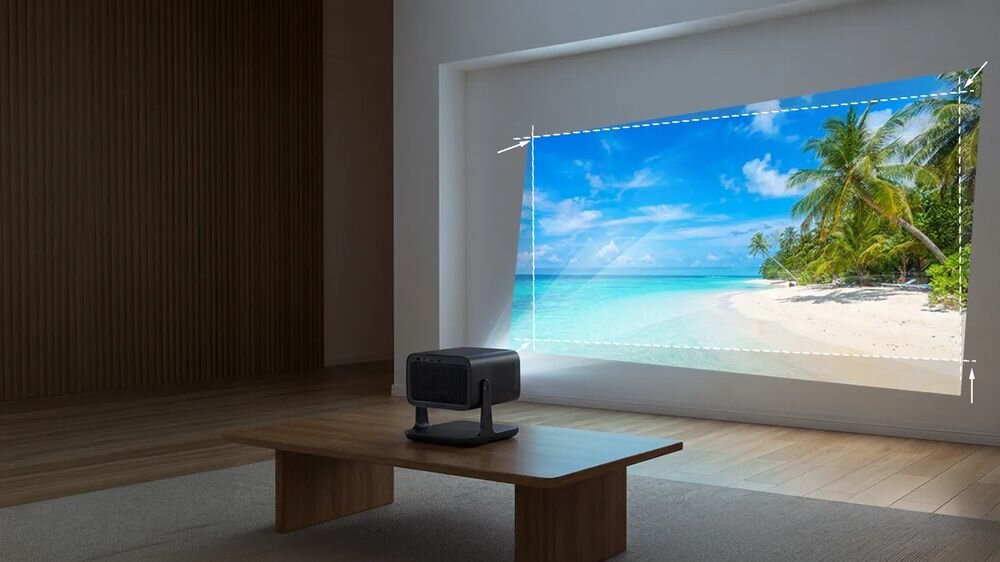 W pomieszczeniu na drewnianym stoliku znajduje się projektor, który wyświetla obraz tropikalnej plaży na ścianie. Obraz jest otoczony przerywaną linią wskazującą obszar projekcji.