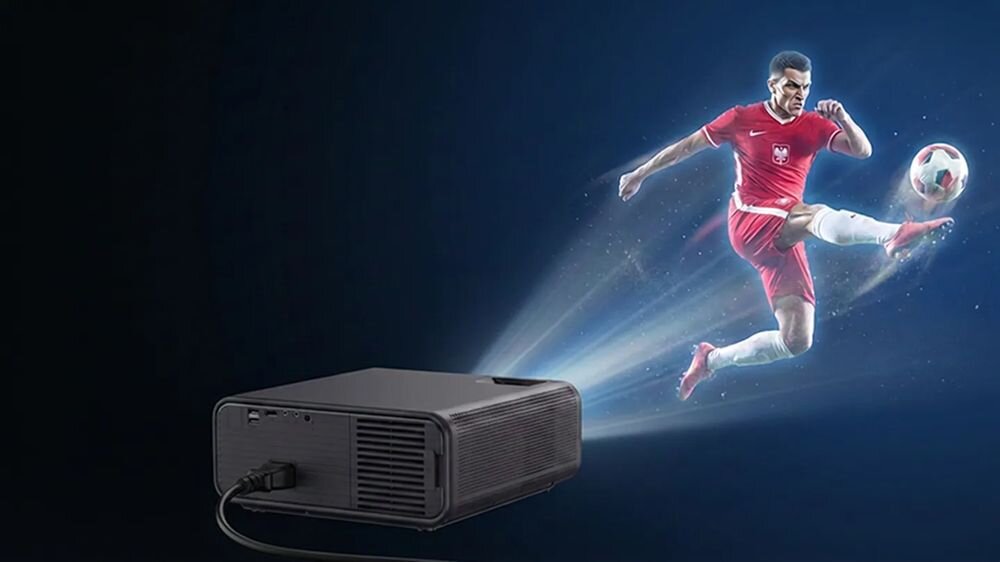 Na ciemnym tle widoczny jest projektor, z którego emitowane jest światło przedstawiające piłkarza w czerwonym stroju kopiącego piłkę. Projektor jest czarny i ma widoczny kabel zasilający.