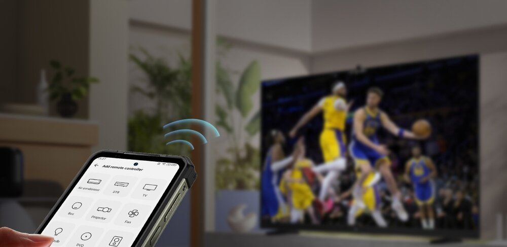 Smartfon z włączoną aplikacją do zdalnego sterowania, na ekranie widoczne ikony funkcji. W tle telewizor wyświetlający mecz koszykówki.