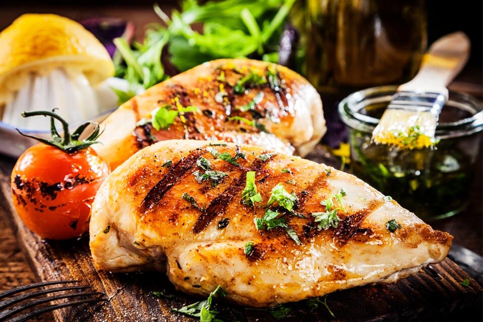 3 poziomy mocy grilla Na drewnianej desce znajdują się dwa kawałki grillowanego kurczaka posypane ziołami, obok leży grillowany pomidor. W tle widoczna jest połówka cytryny oraz słoik z zielonym sosem i pędzelkiem.