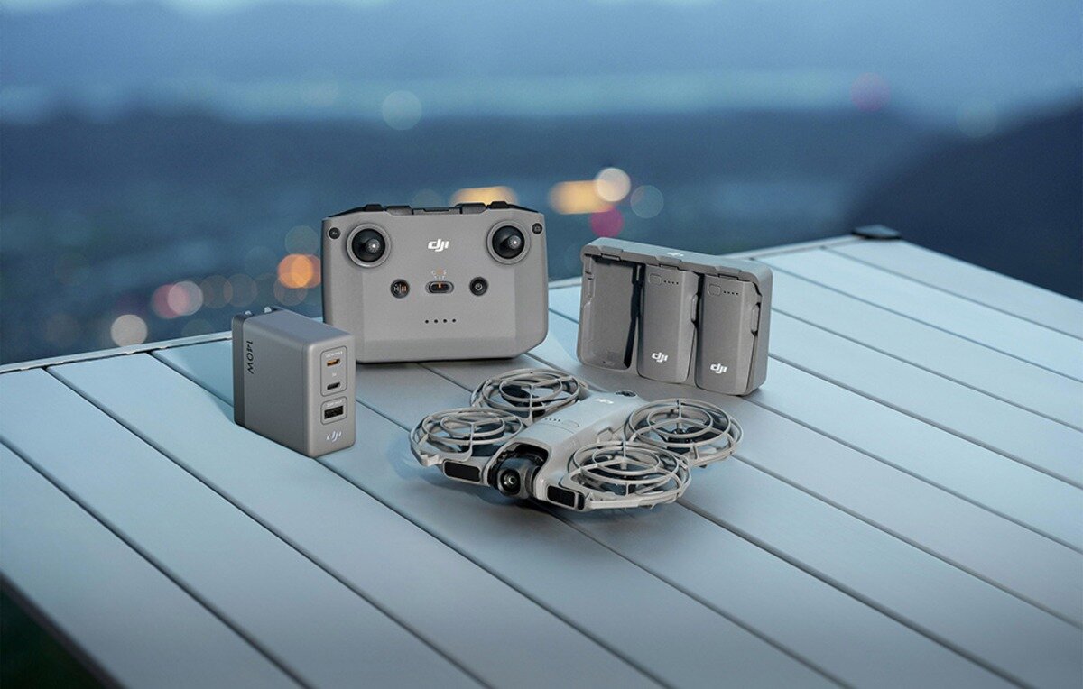 Dron DJI z kontrolerem, bateriami i ładowarką na metalowym stole w plenerze