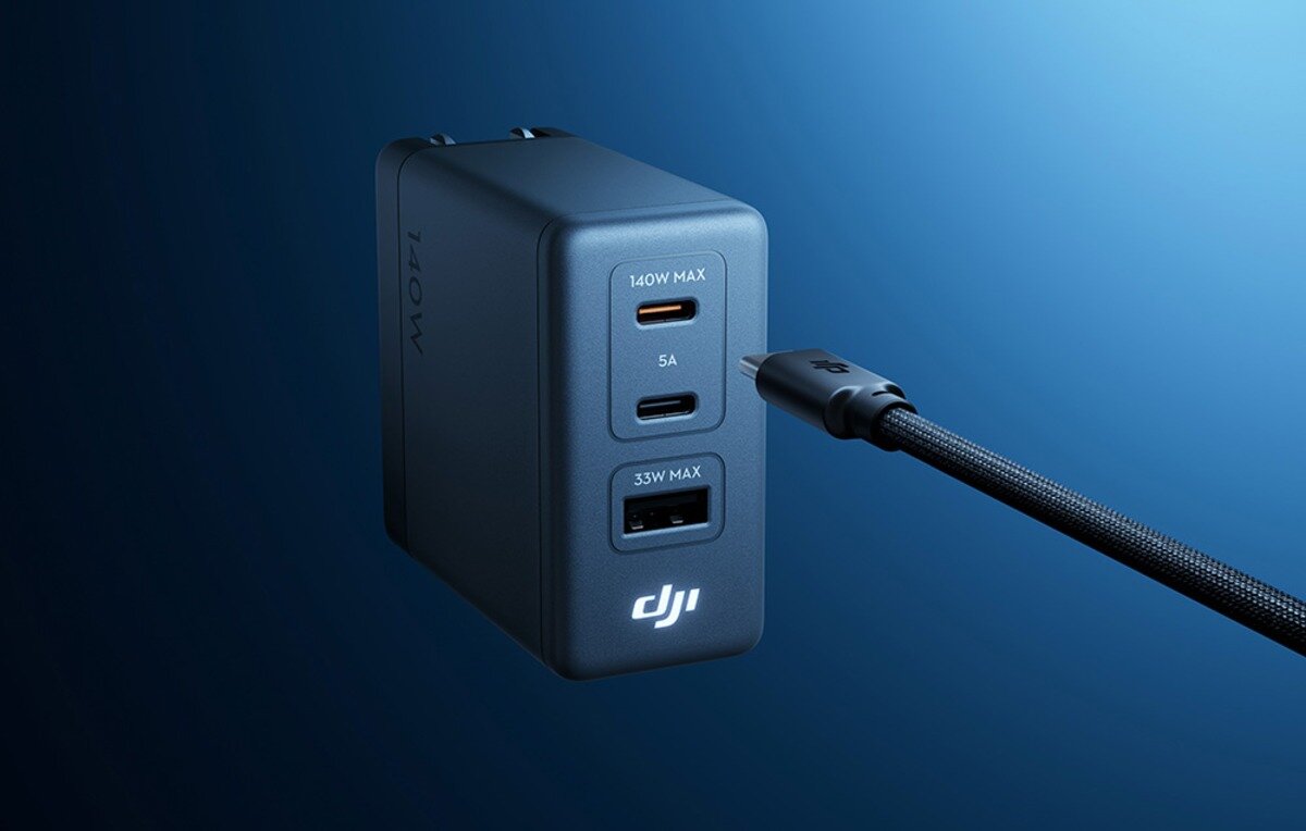 Szara ładowarka sieciowa DJI 140W z portami USB i podłączonym czarnym kablem na niebieskim tle