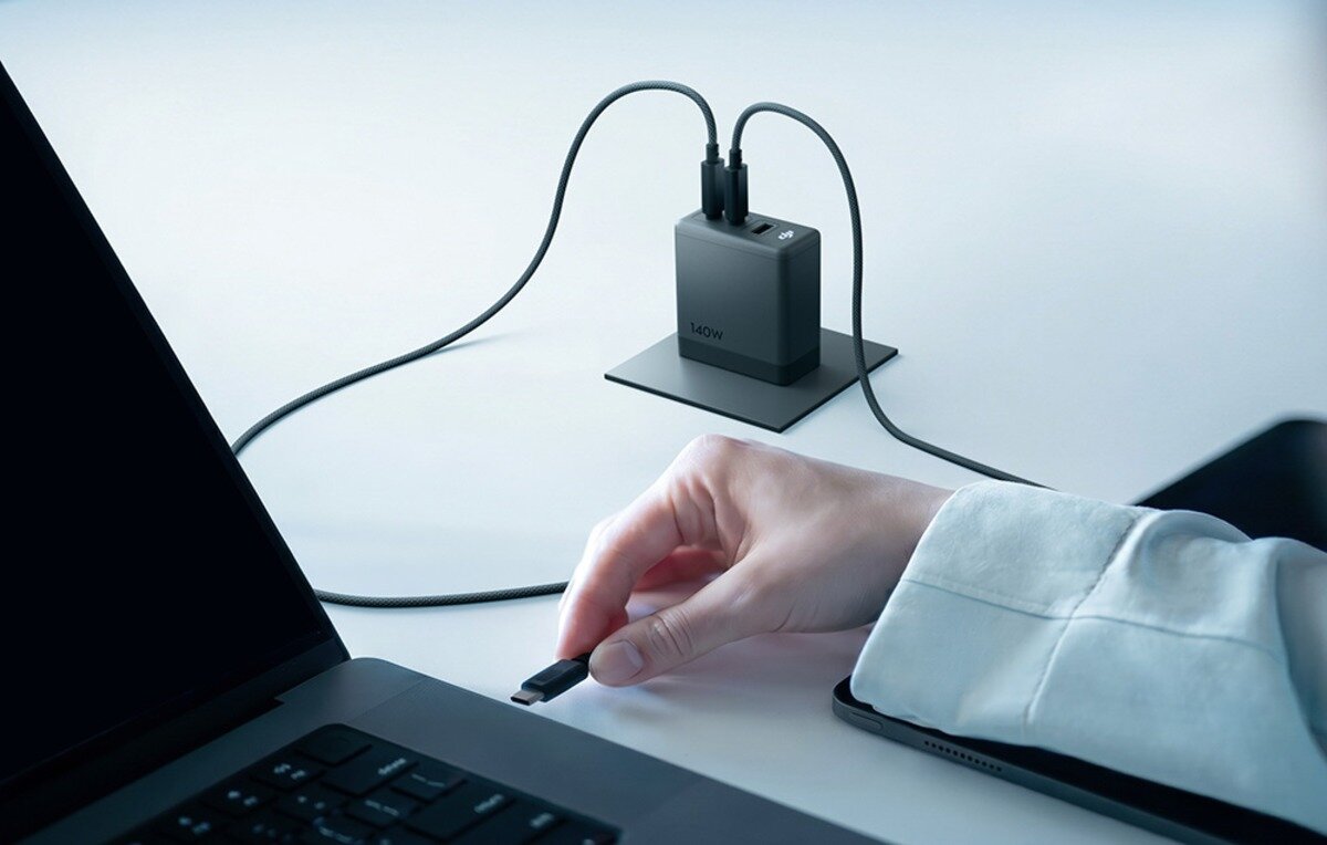 Ręka podłączająca kabel z ładowarki DJI 140W do laptopa na jasnym biurku