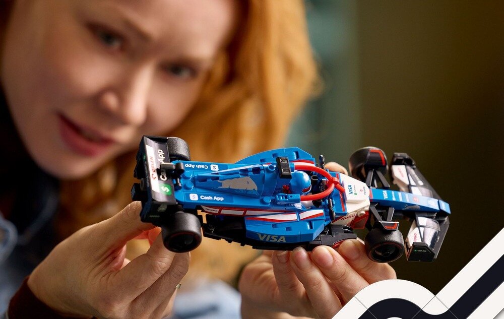 Osoba trzyma model bolidu F1 z klocków LEGO w kolorach niebieskim, czarnym i białym z widocznymi napisami \'Visa\' i \'Cash App\'.