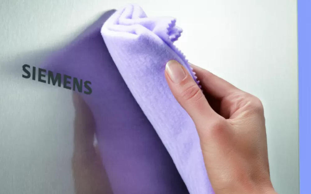 Osoba przeciera fioletową ściereczką powierzchnię z logo \'SIEMENS\'.
