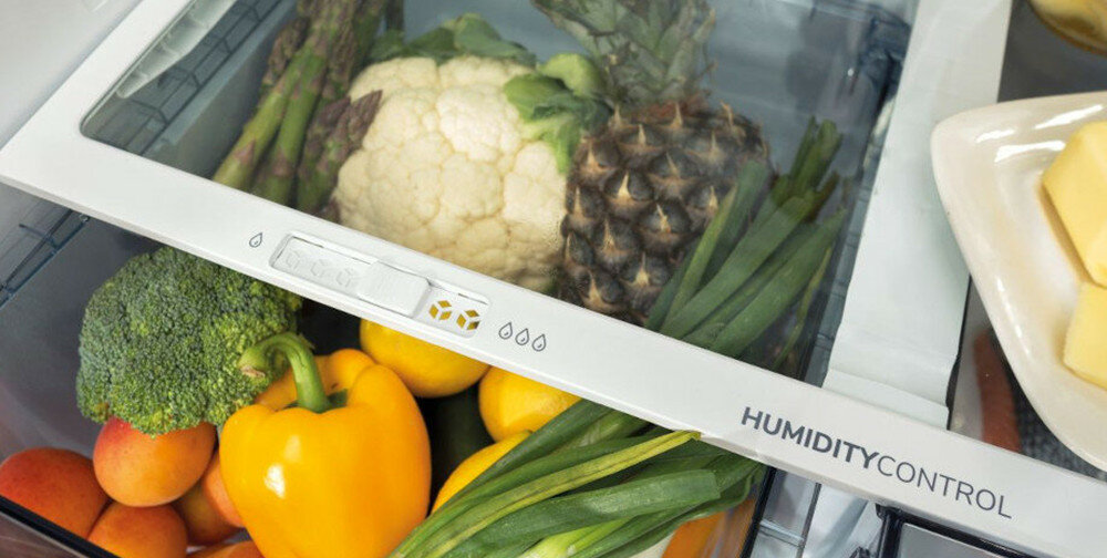 Wnętrze lodówki z widocznymi warzywami i owocami, takimi jak kalafior, ananas, papryka i brokuł. Na szufladzie napis \'HUMIDITY CONTROL\'.