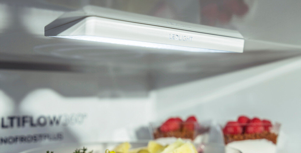Wnętrze lodówki z widocznym oświetleniem LED i półką z deserami. Na ścianie lodówki widoczny jest napis \'MULTIFLOW 360° NO FROST PLUS\'.