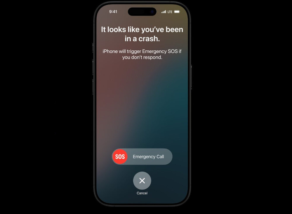 Na ekranie smartfona widoczny jest komunikat: \'It looks like you’ve been in a crash. iPhone will trigger Emergency SOS if you don’t respond.\' Poniżej znajduje się przycisk \'SOS Emergency Call\' oraz opcja \'Cancel\'.