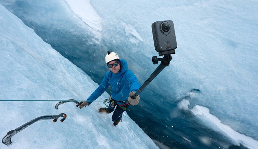 Kamera sportowa DJI Osmo 360 II Wspinacz w kasku i okularach na lodowcu trzyma kijek z małym urządzeniem skierowanym w swoją stronę