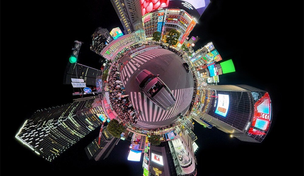 Kamera sportowa DJI Osmo 360 II Panoramiczne ujęcie skrzyżowania w mieście nocą z perspektywy 'efektu małej planety', widoczne wieżowce i światła